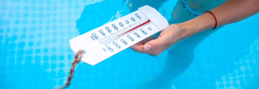Hand hält Thermometer in blauem Poolwasser